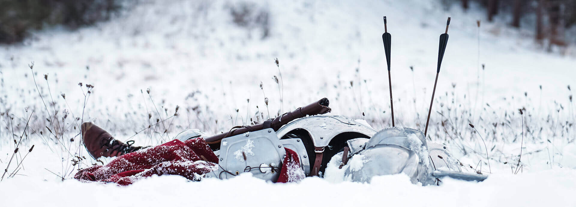 A fallen knight's armor and sword covered in snow, surrounded by a winter landscape.