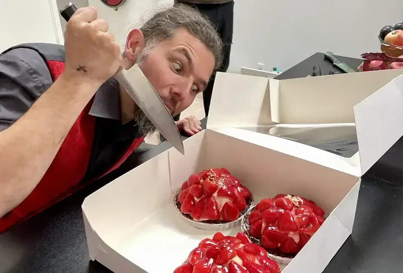 Excited man in red vest preparing to cut into delicious strawberry desserts in a bakery box.