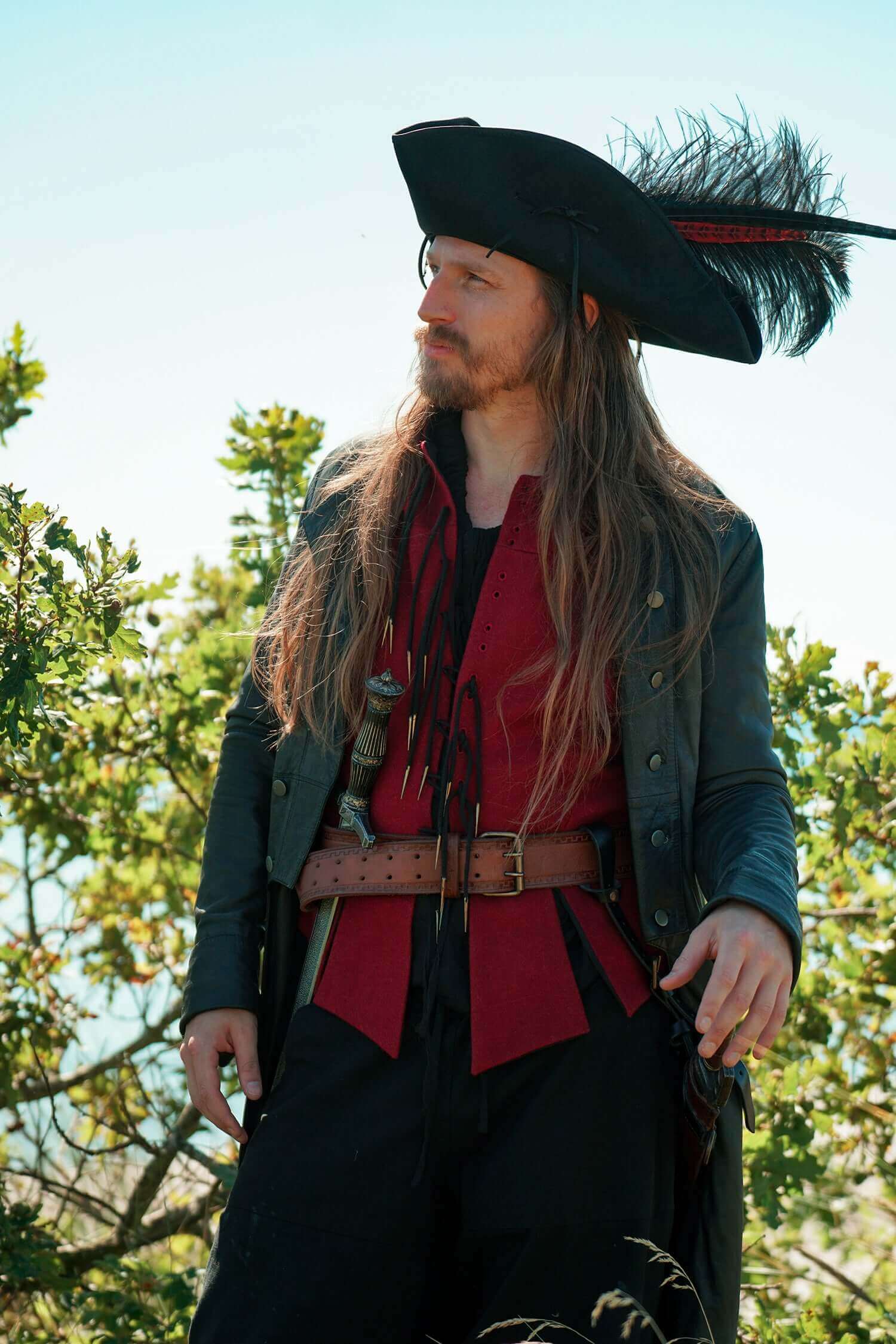 Person in pirate costume with tricorn hat and red shirt standing outdoors.