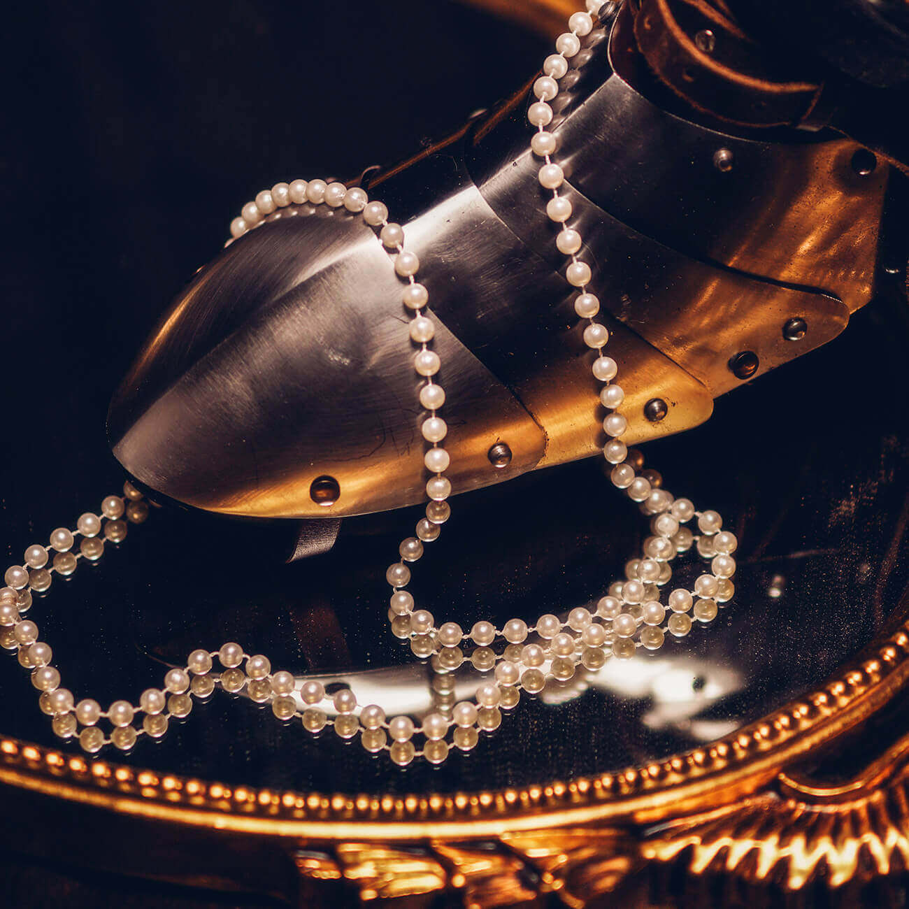 Close-up of a metallic boot with pearls draped over it on a reflective surface.