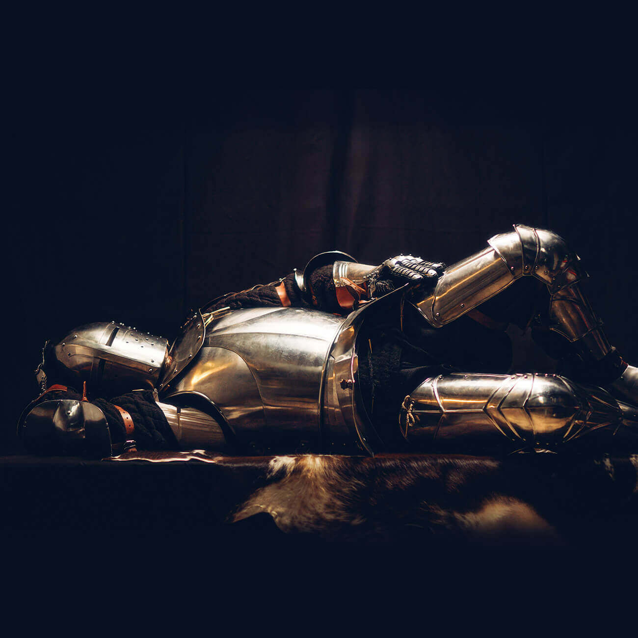 A medieval knight's suit of armor resting on a dark background, showcasing intricate details of the metalwork.