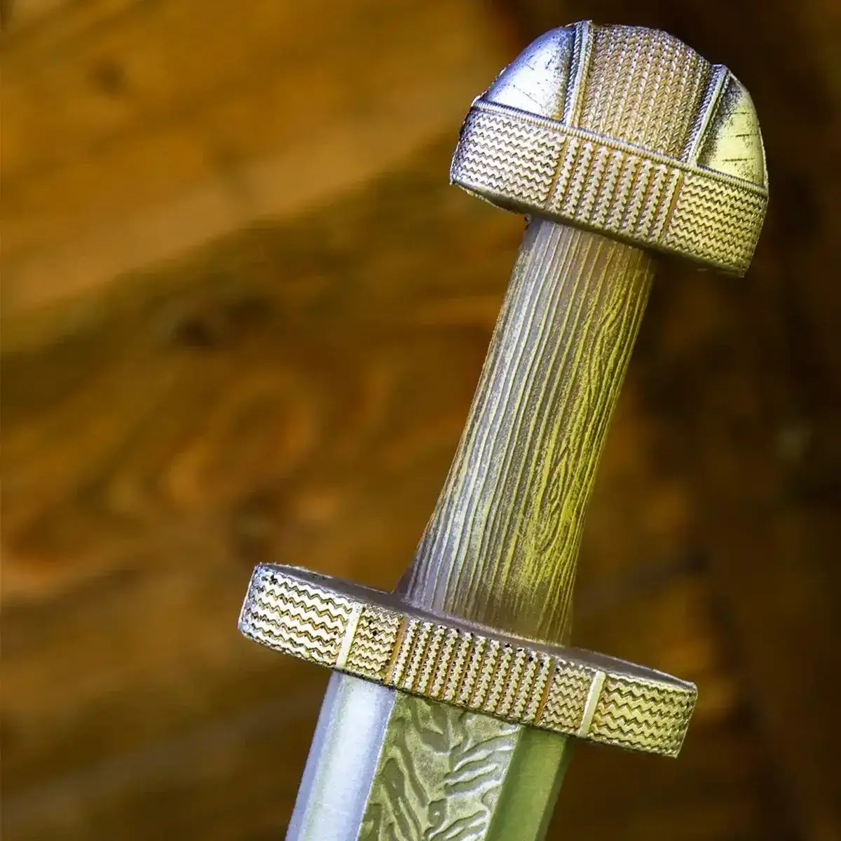 Close-up of a decorative sword's hilt with intricate detailing against a warm wood background.