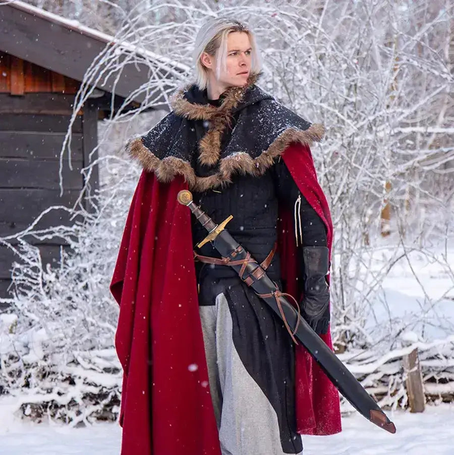 A warrior in a red cloak and fur trim stands in a snowy landscape, holding a sword in a wintery forest setting.