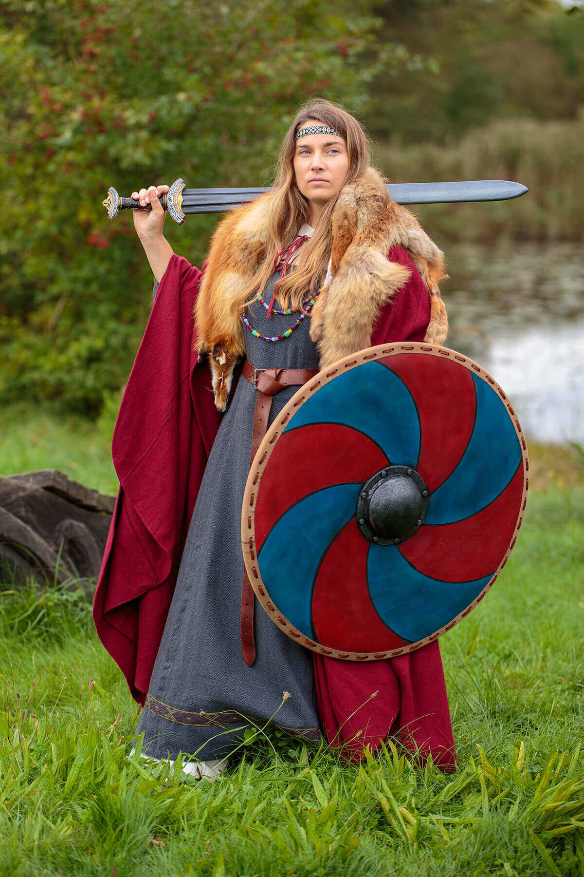 Person in Viking attire holding a sword and shield in a natural setting