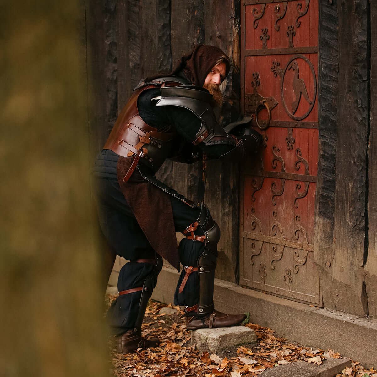 A medieval warrior in armor trying to open a rustic wooden door, set in an outdoor environment.