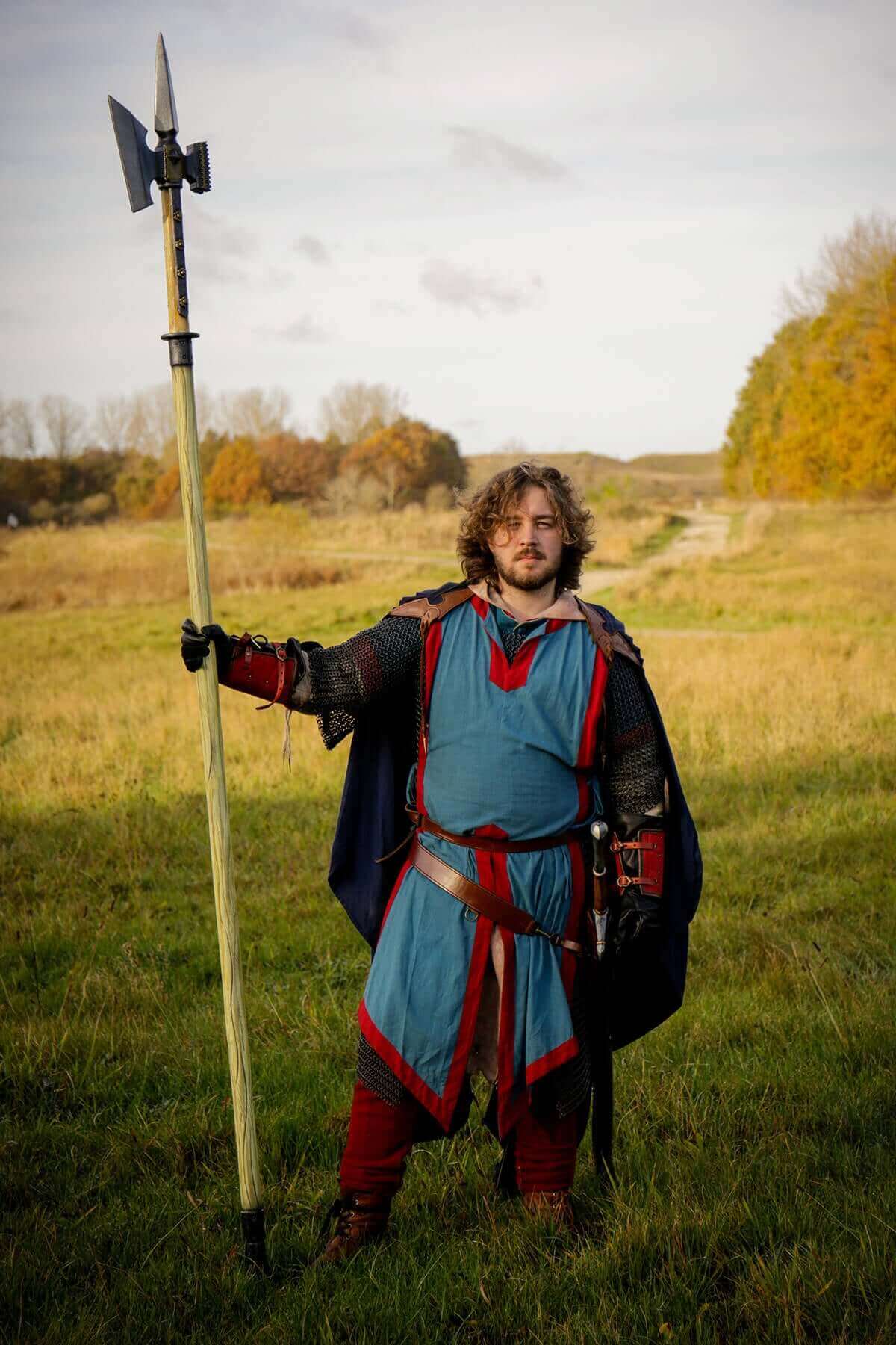 Man in historical warrior costume holding a poleaxe in an open field