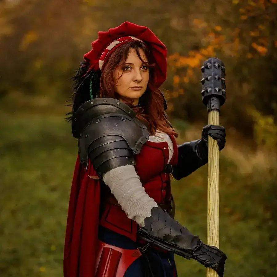 Fantasy-themed portrait of a woman in a red cloak and armor, wielding a staff in a picturesque outdoor setting.