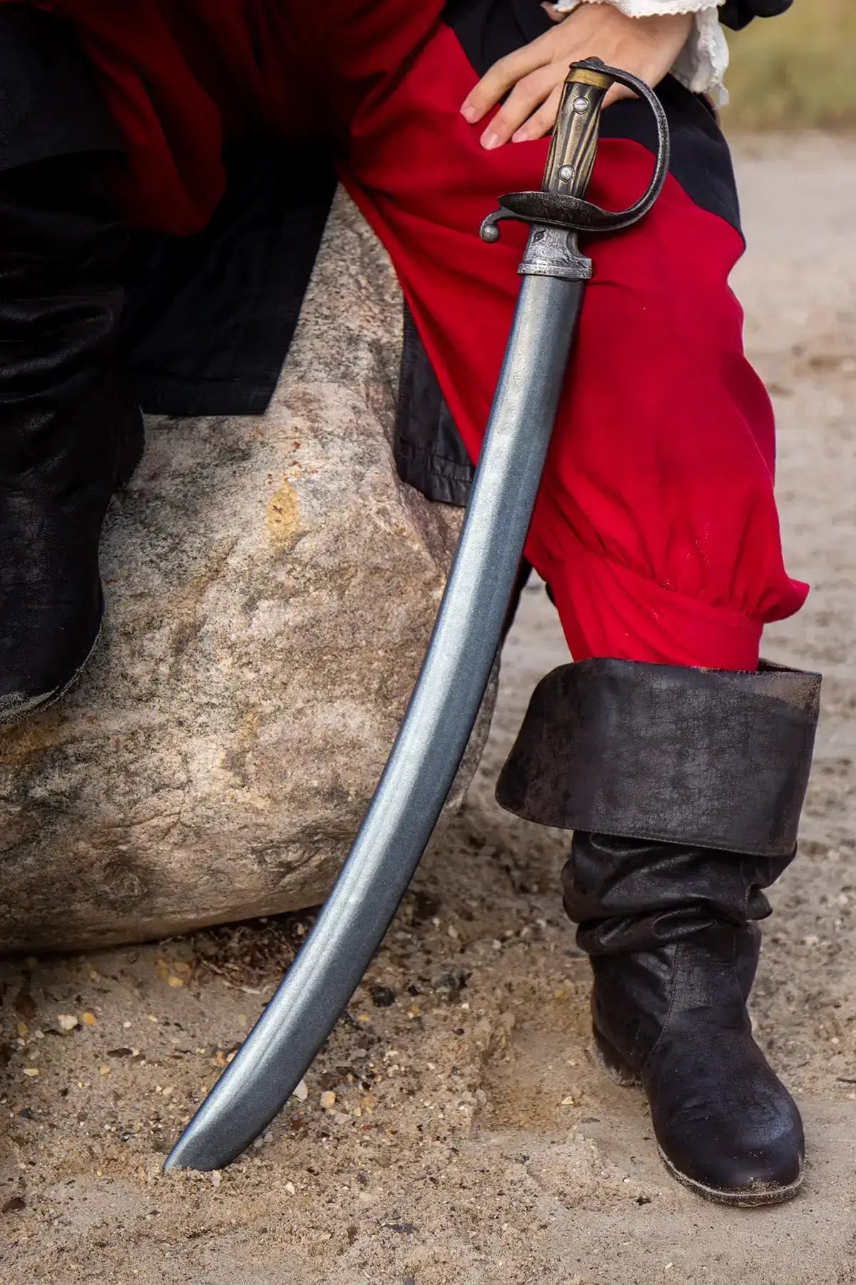 Close-up of a pirate sword resting on a rock, with a pirate dressed in traditional attire in the background.