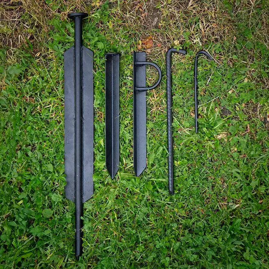 Set of black metal ground stakes and tools arranged on green grass, ideal for camping or outdoor activities.