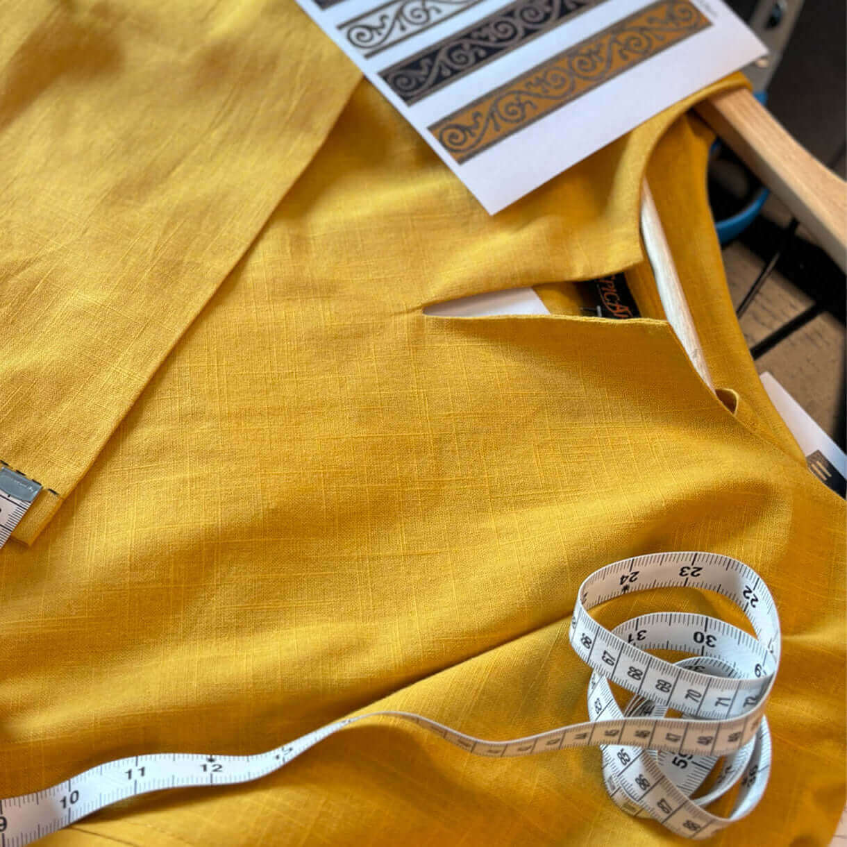 A seamstress measuring fabric on a yellow garment using a measuring tape, showcasing sewing and design skills.