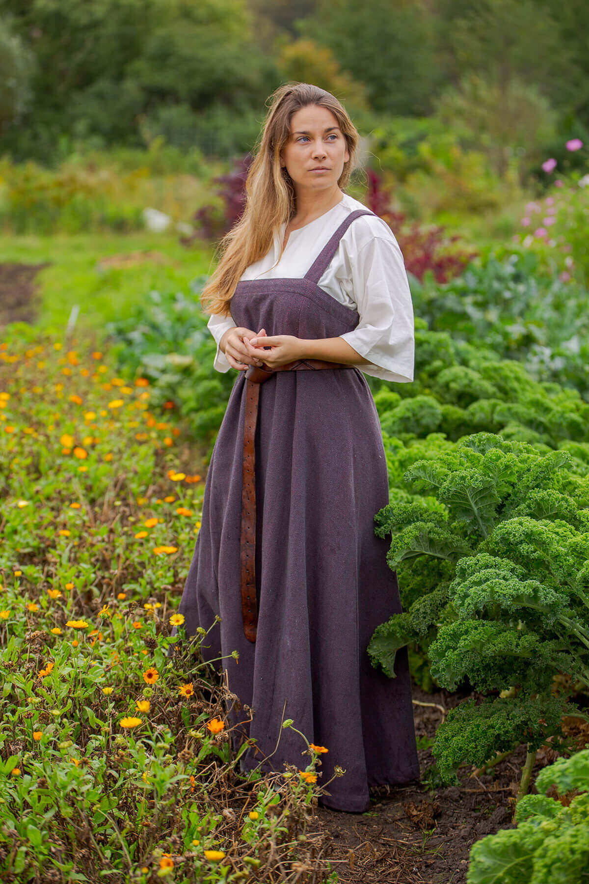 Woman in a purple dress standing in a garden with greenery and flowers.
