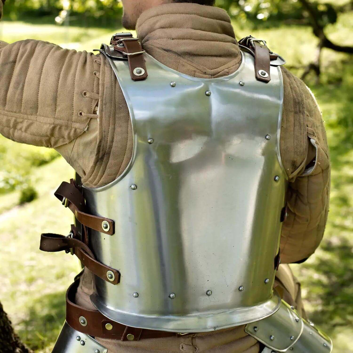 Close-up of a metallic armor vest showing leather straps, worn by a person in an outdoor setting.