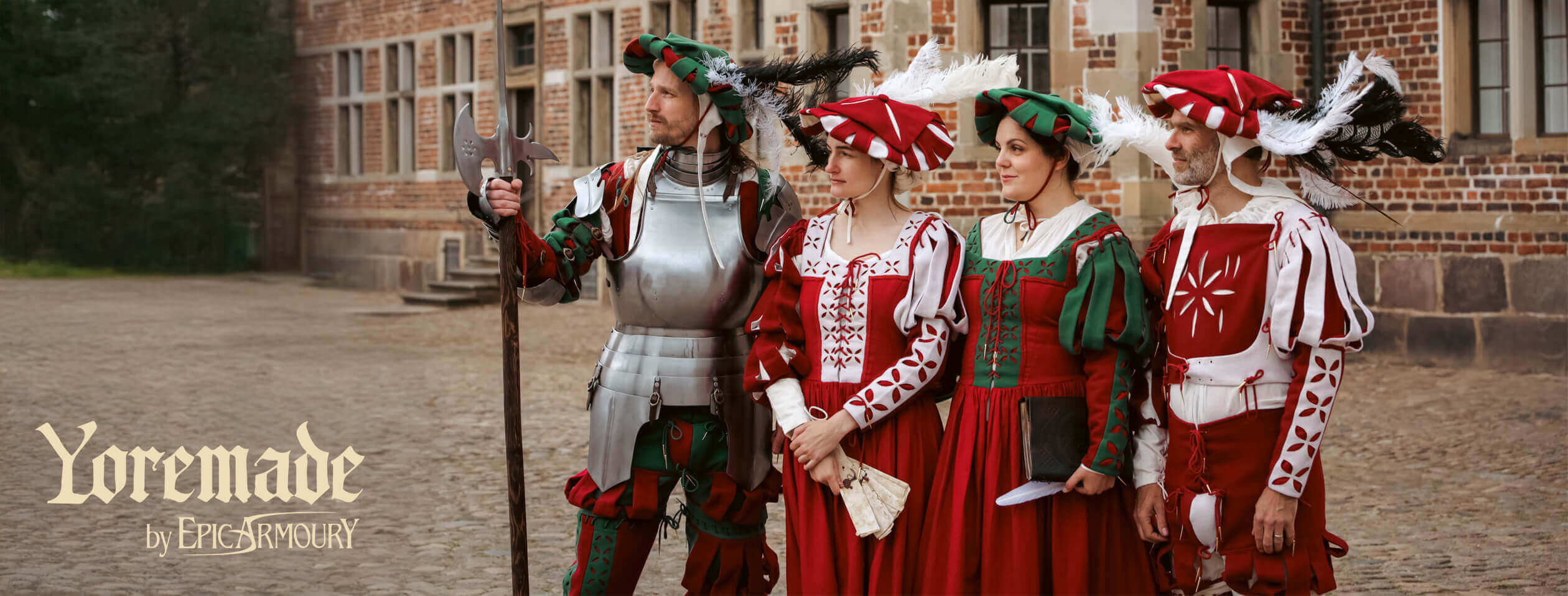 Four people in historical costumes stand outside a building, showcasing vibrant red and green attire.