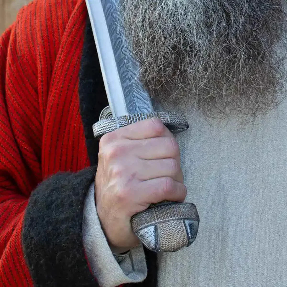 Close-up of a hand gripping The EirikR Sword, showcasing its intricate hilt and design elements.