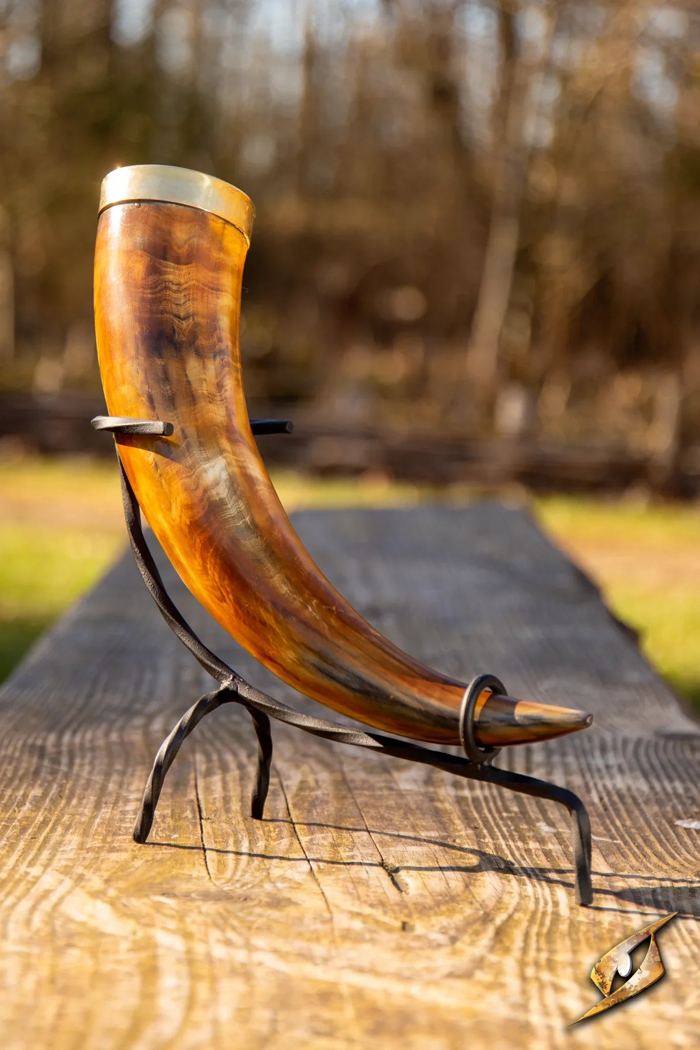 Brown drinking horn with golden trim on a wooden bench with a forest backdrop