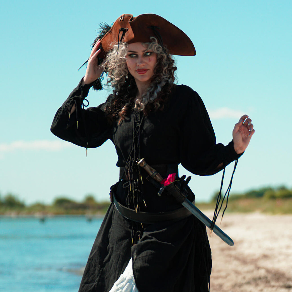 Womens Pirate Costumes with a model wearing a pirate hat and accessories by the beach.