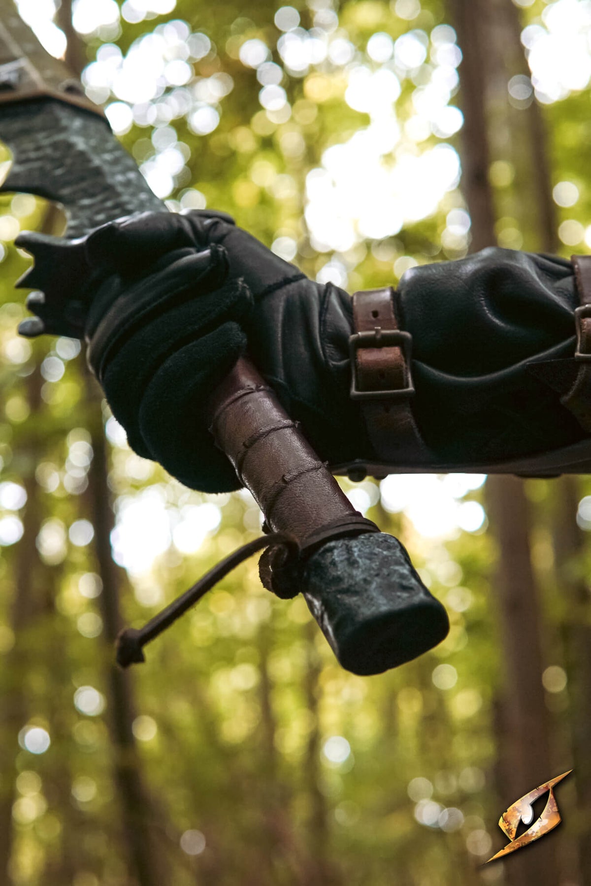 A close-up of a hand wearing a black leather glove holding the handle of a bow, with a blurred forest background.