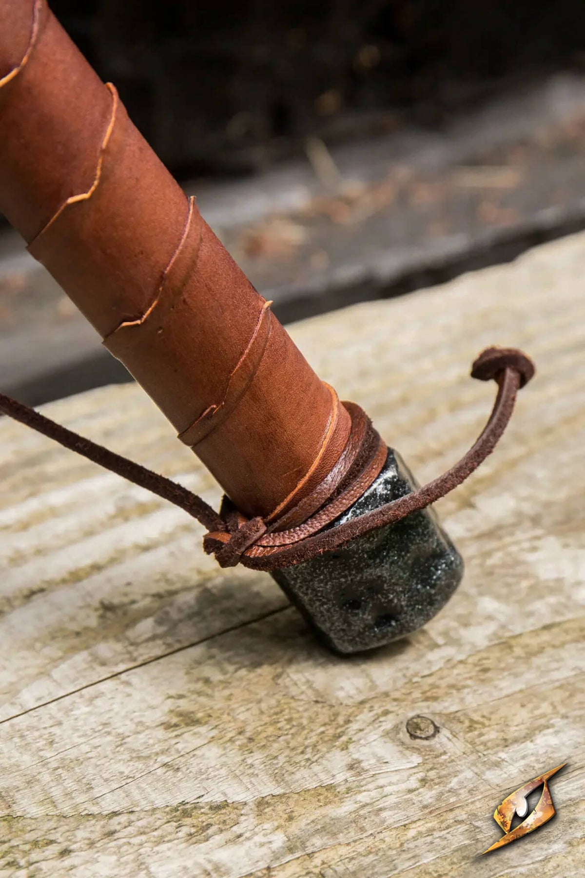 A close-up of a leather-wrapped wooden pole or handle secured with a leather cord around a dark stone or metal base, resting on a weathered wooden surface.