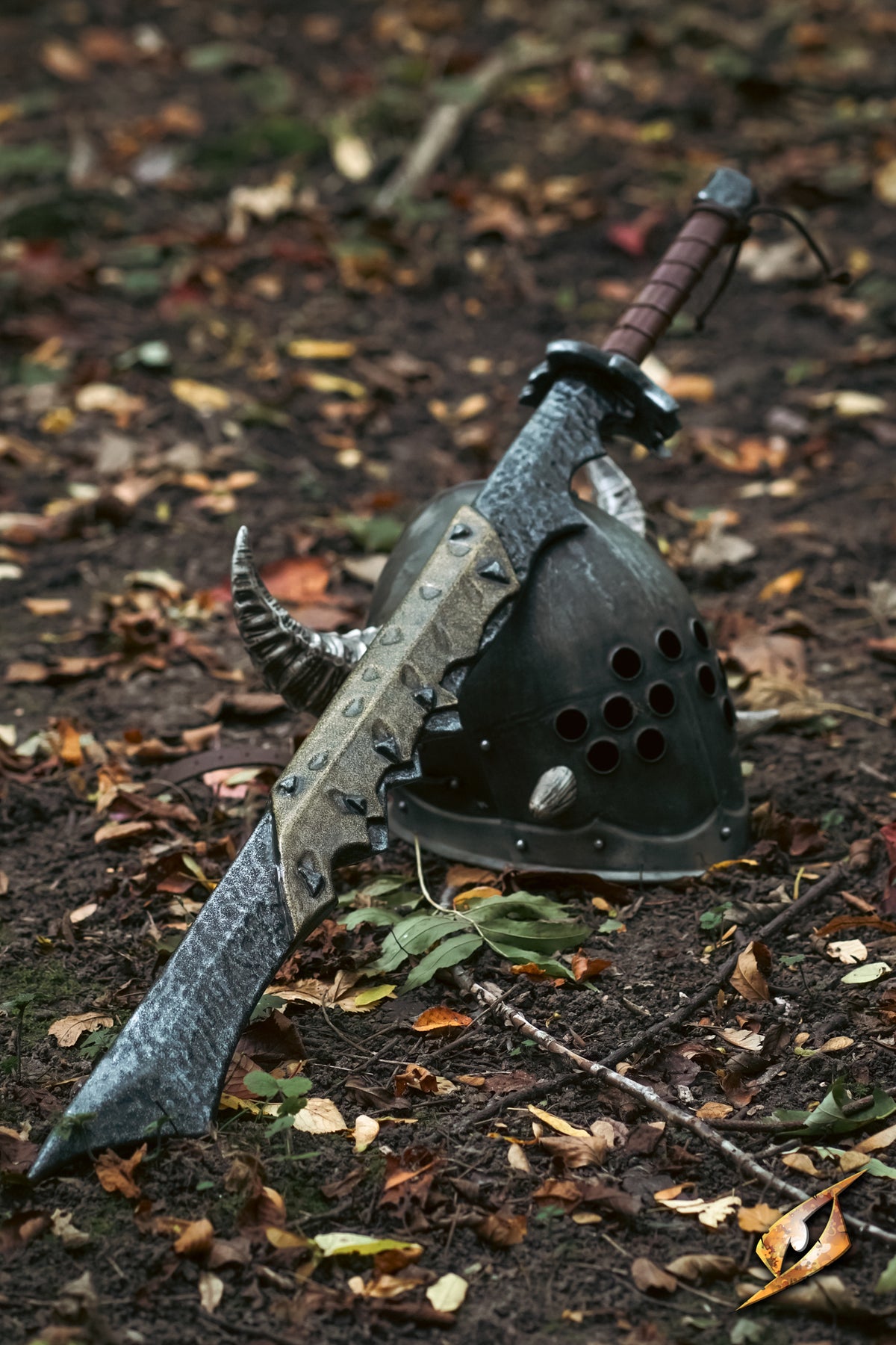 A fantasy sword with a textured silver-gray blade and a brown wrapped hilt, resting on a dark metal horned helmet placed on a forest floor covered in fallen leaves.