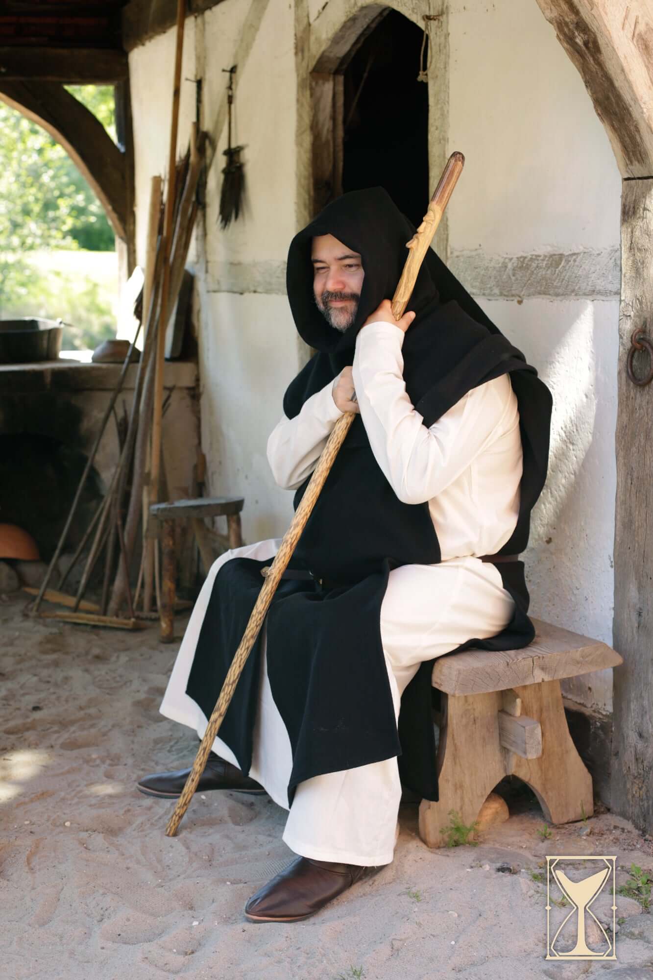 A man wearing a Simple Liripipe Hood - Brushed Wool sitting with a staff, embodying medieval style.