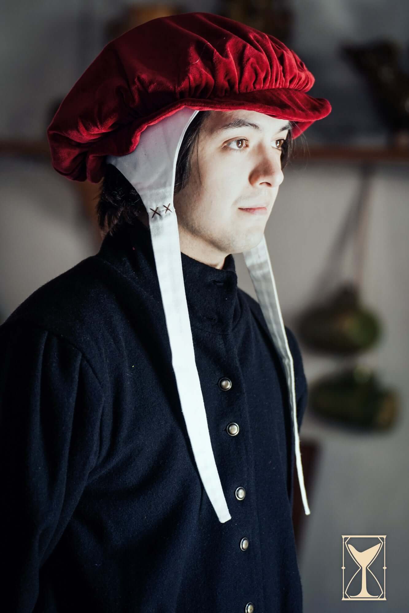 Man wearing a traditional red Surcoat Lorenzo hat with white ties, showcasing historical fashion.