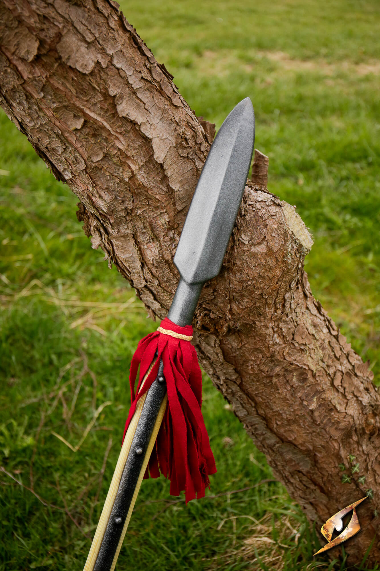 Landsknecht Pike leaning against a tree with a red tassel on its shaft, captured in a green field.