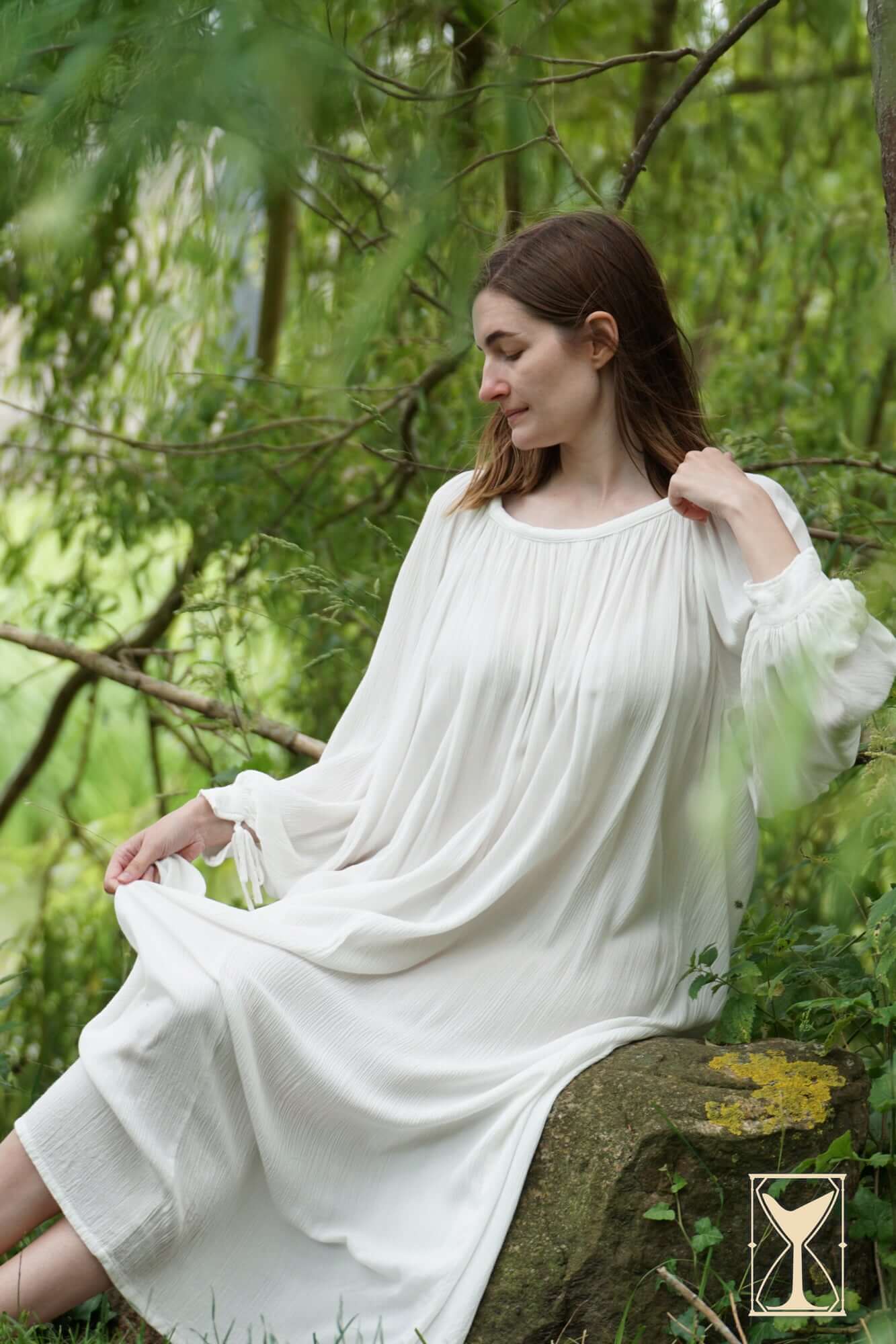 Model wearing the Shift Giulia, a historical costuming garment, sitting on a rock surrounded by greenery.