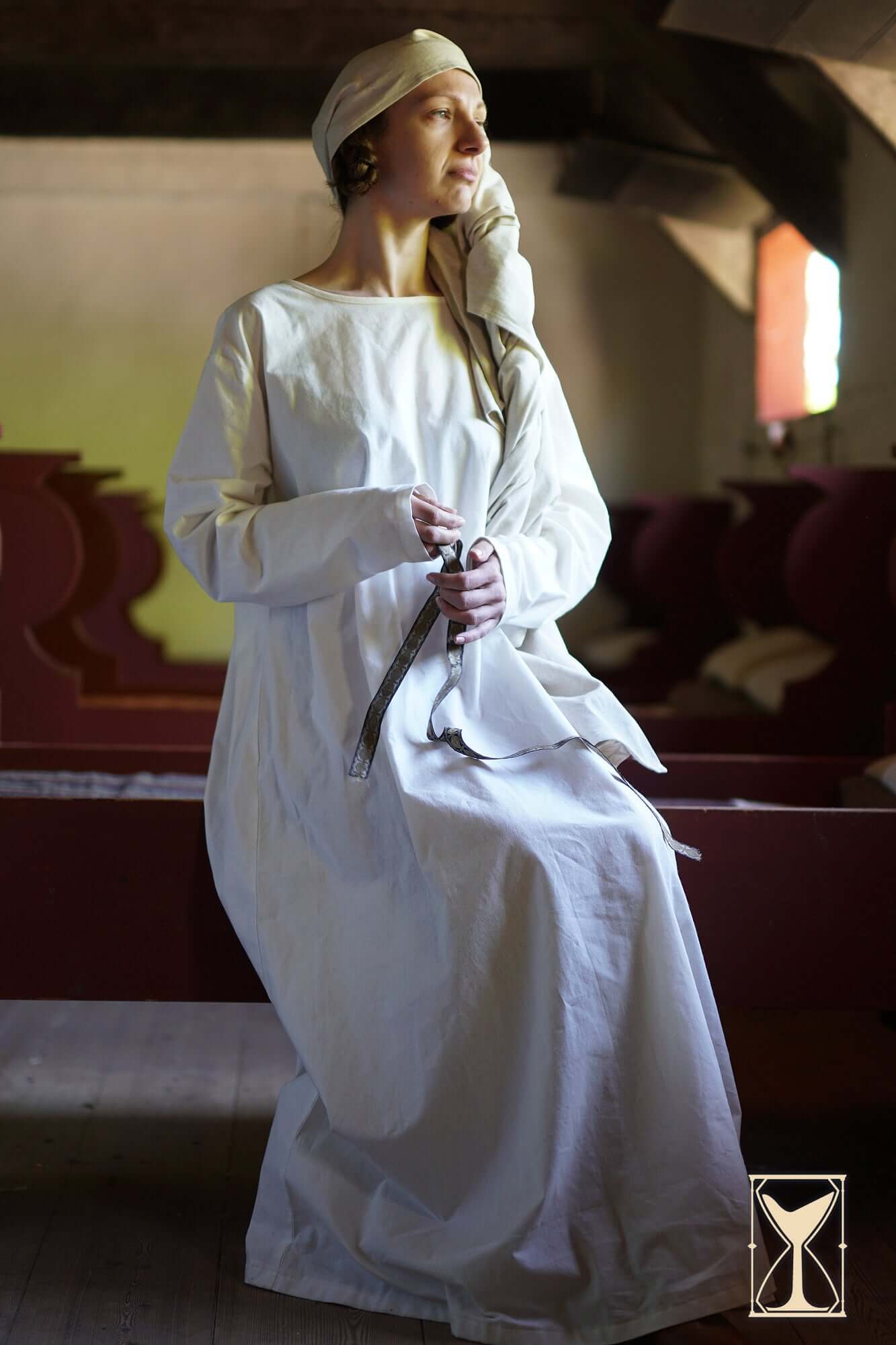 Woman seated in a white Undertunic Modesto, showcasing a medieval historical silhouette.