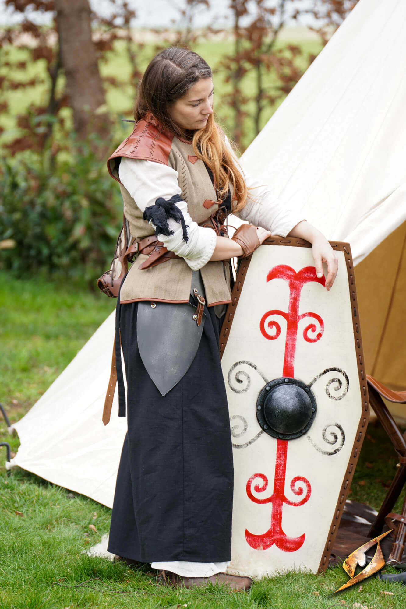 A woman in medieval attire stands beside a Germanic Shield, showcasing its tribal markings and design.