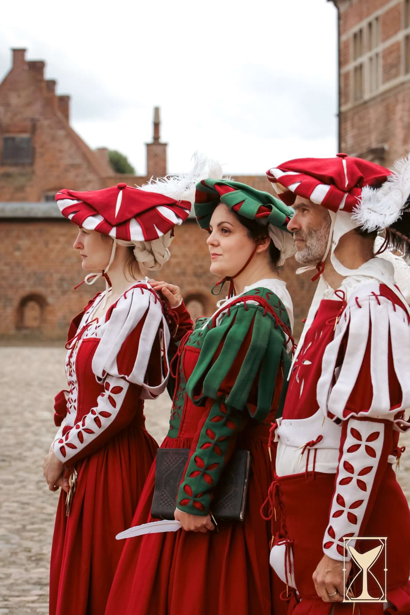 Three individuals dressed in vibrant Renaissance attire wearing Landsknecht Hats with distinct colors and feather accents.