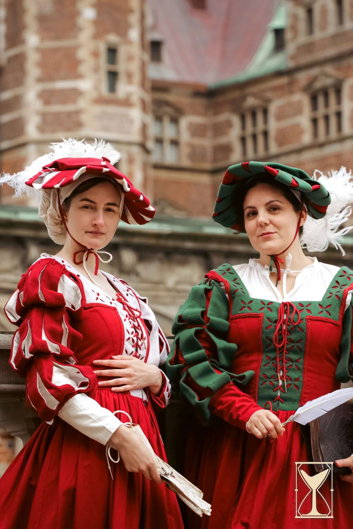Two women in vibrant red Renaissance dresses and hats, showcasing historical fashion elegance.