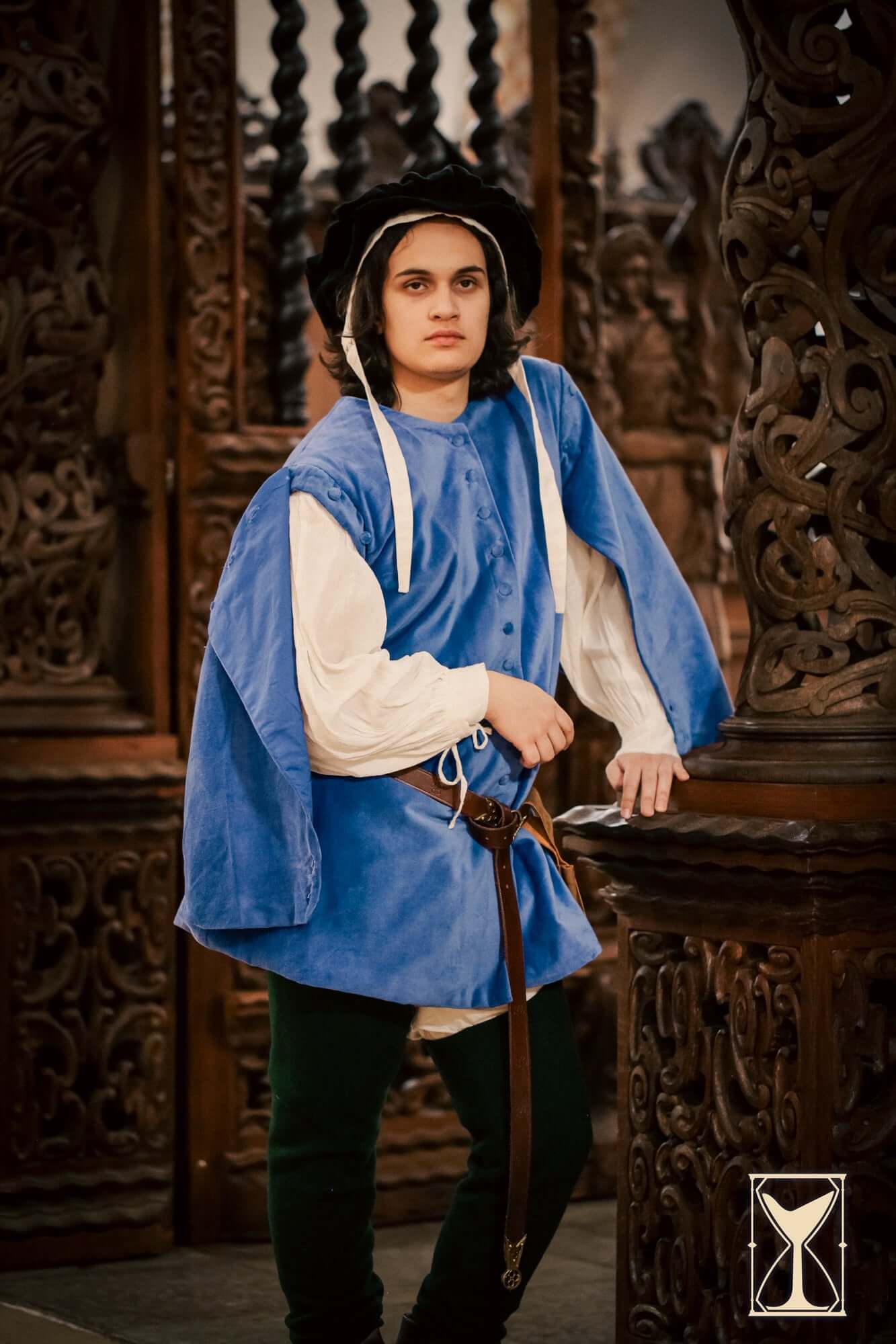 Model wearing a blue Velvet Surcoat, showcasing medieval style and elegance in a historical setting.