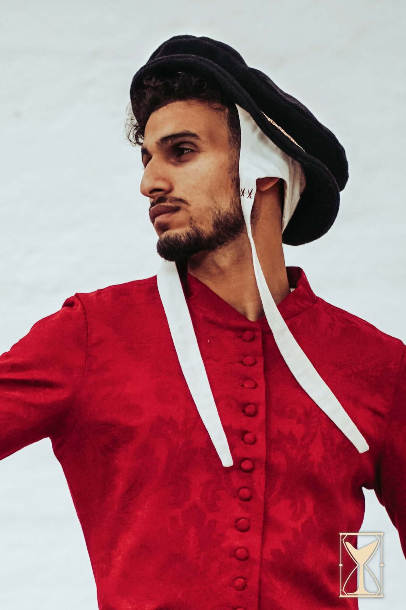 A model wearing the Flat Hat Edward with a red Renaissance-style coat, showcasing 16th-century fashion.