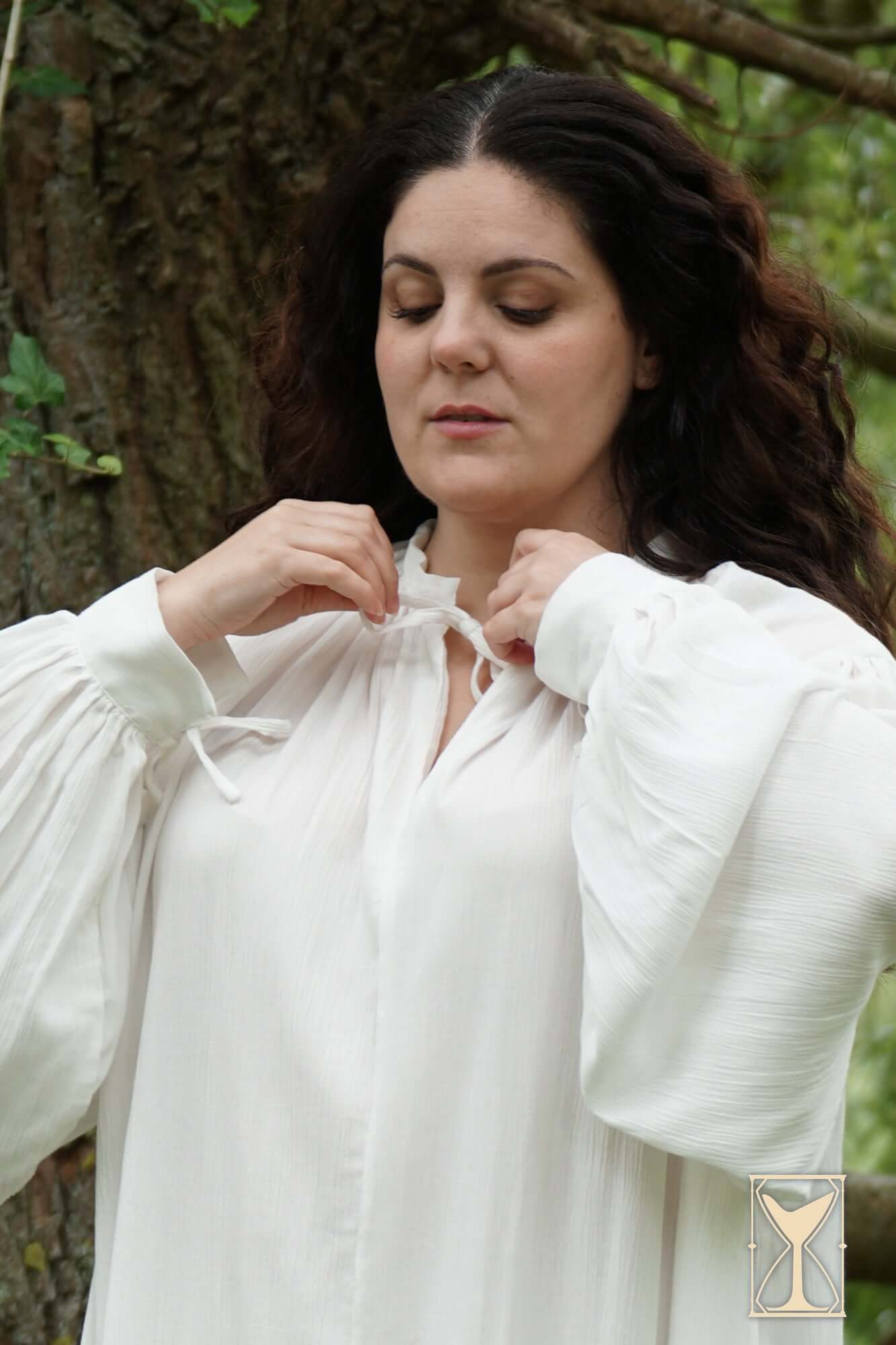 Woman adjusting the ties of the Smock Violet medieval undergarment, showcasing its elegant design in a natural setting.