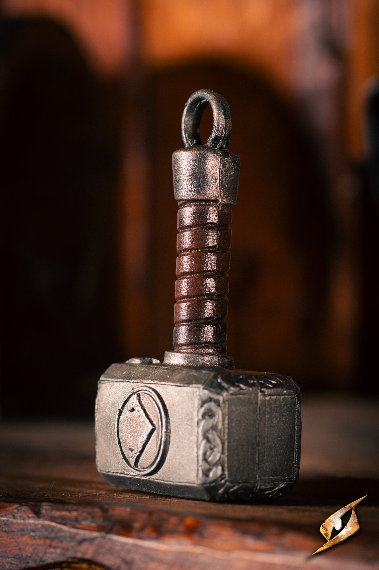 A miniature replica of Thor's hammer, Mjolnir, with a textured dark metallic gray head and a brown wrapped handle, resting on a rustic wooden surface.