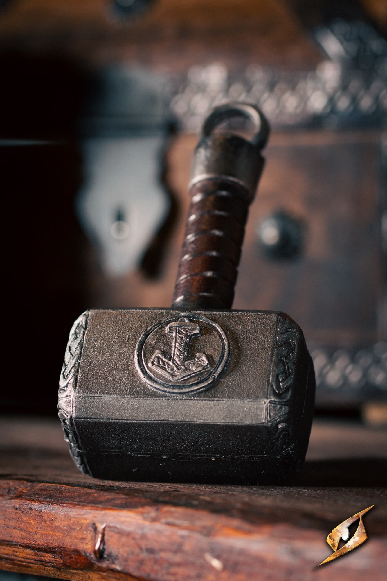 A miniature replica of Thor's hammer, Mjolnir, with a dark metallic head featuring an engraved emblem and a brown wrapped handle, resting on a rustic wooden surface.