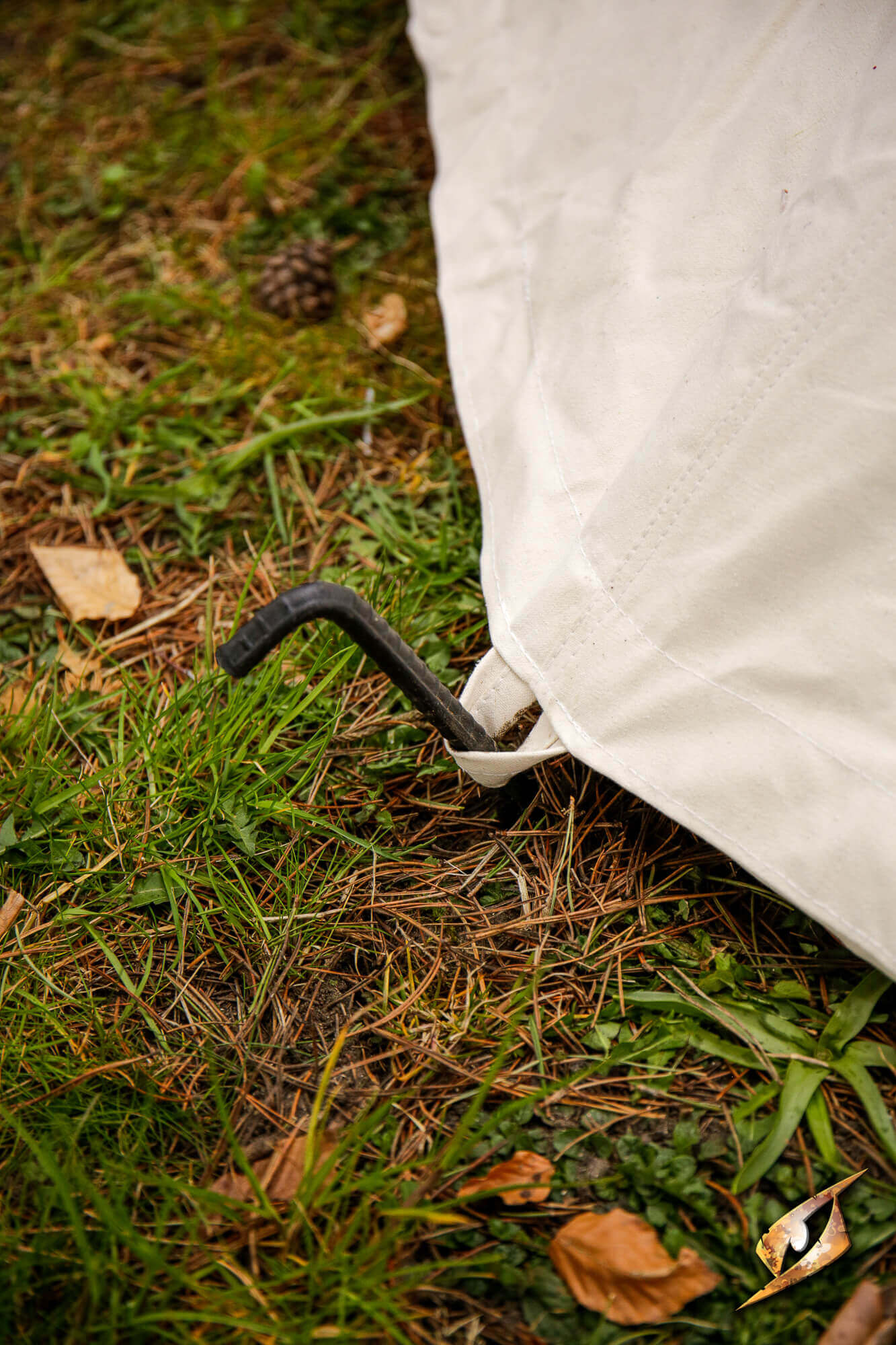Complete Conical Tent - Compact peg secured into the ground on a grassy surface with fallen leaves.