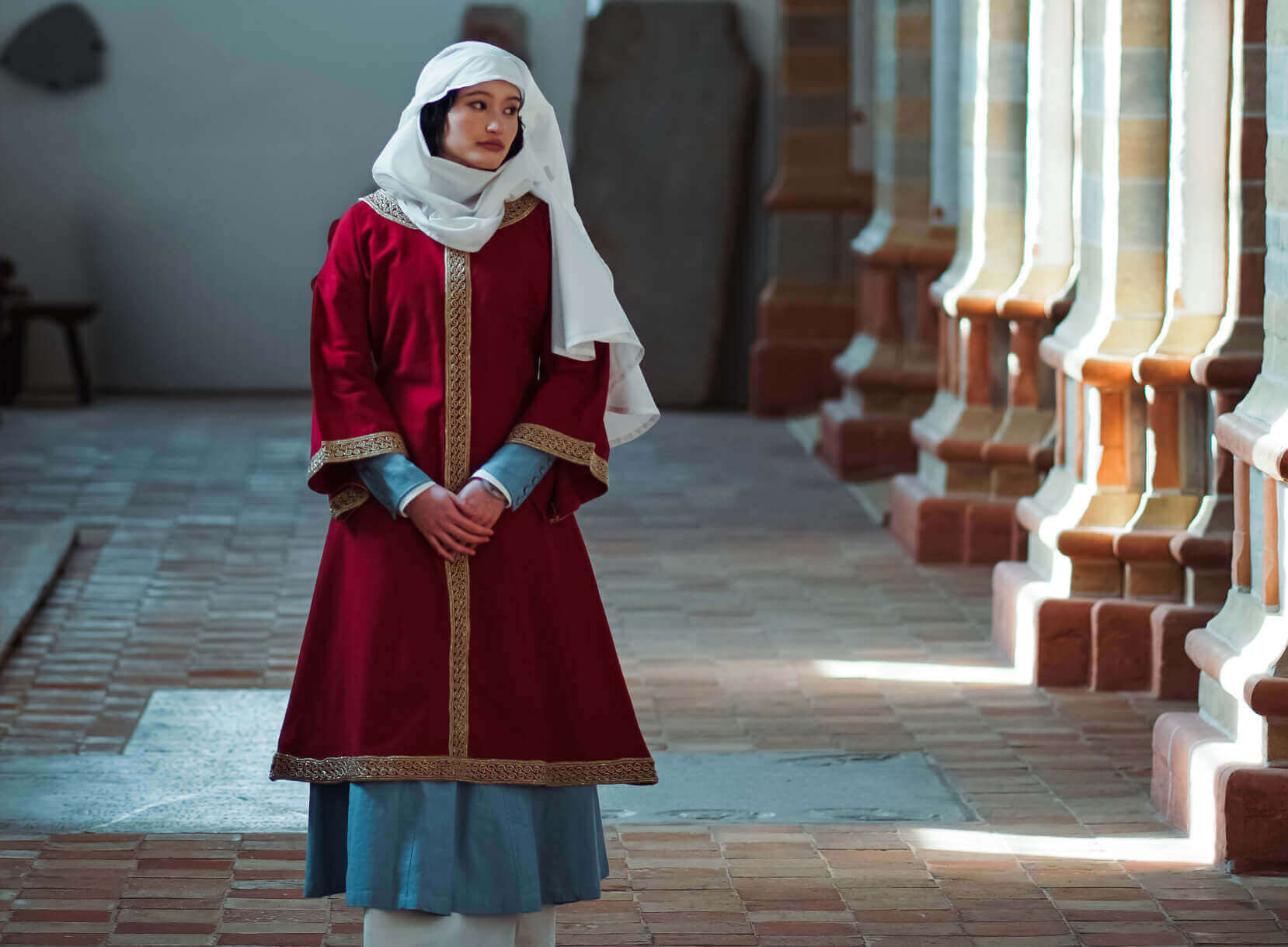 Woman in high medieval red and blue cloak with a white head covering.