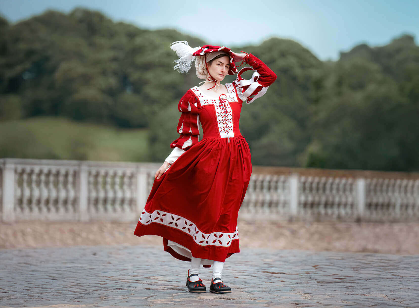 Young woman in a vibrant red dress with white accents, standing outdoors, showcasing elegant traditional fashion.