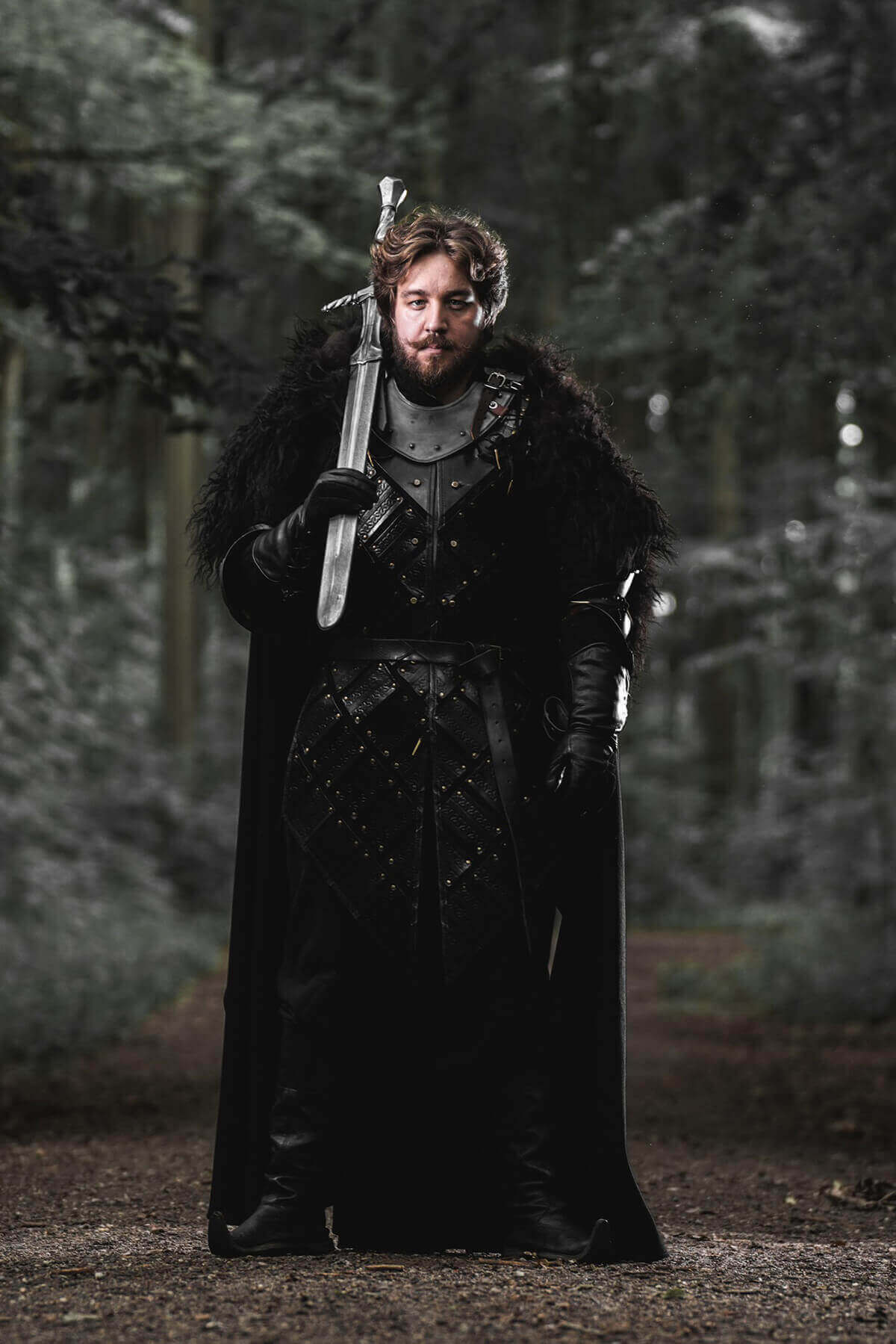 Person in dark medieval attire holding a sword in a forest setting