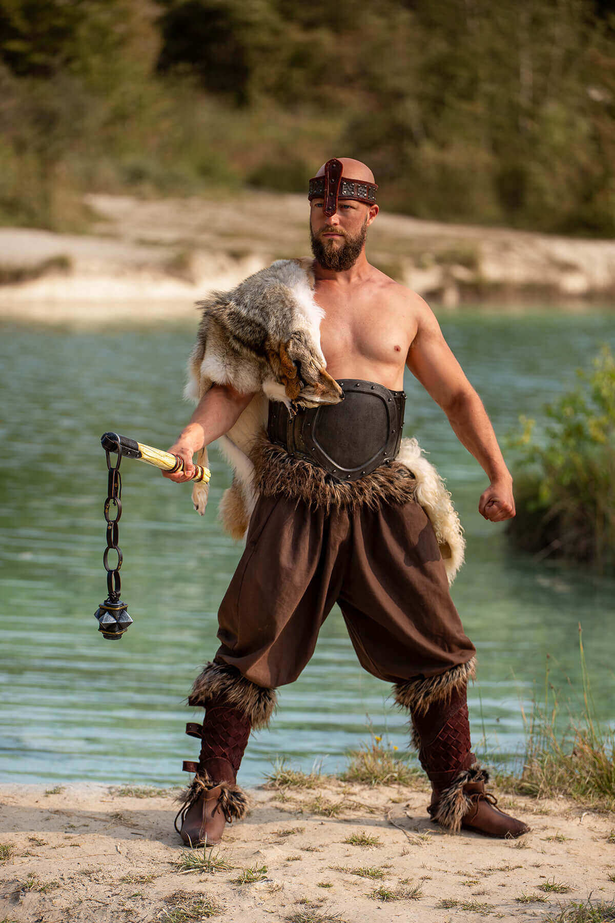 Man in fantasy costume holding a weapon by a body of water.