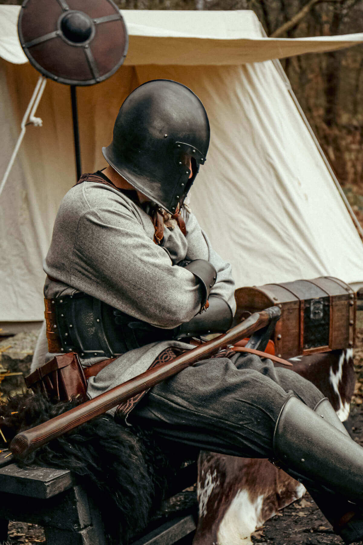 Person in larp clothes and armor sitting in front of a tent in a forest setting