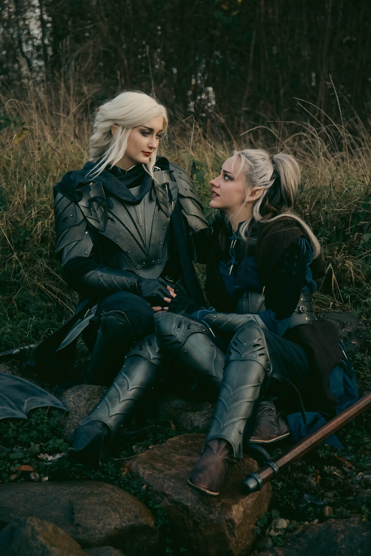 Two people in fantasy costumes sitting on a log in a forest setting.