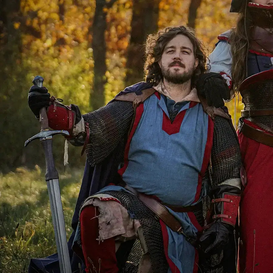 Knight in historical armor, seated with sword, surrounded by autumn foliage, showcasing medieval attire.