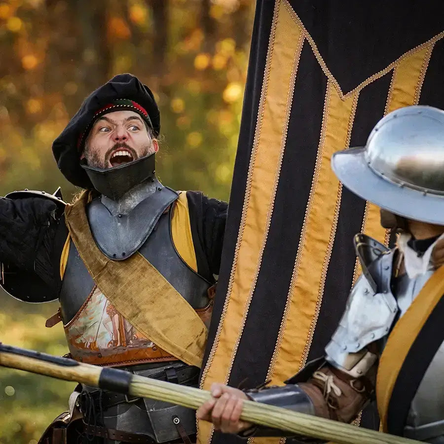Excited medieval reenactors in armor, waving flags and smiling during a historical battle event in autumn.
