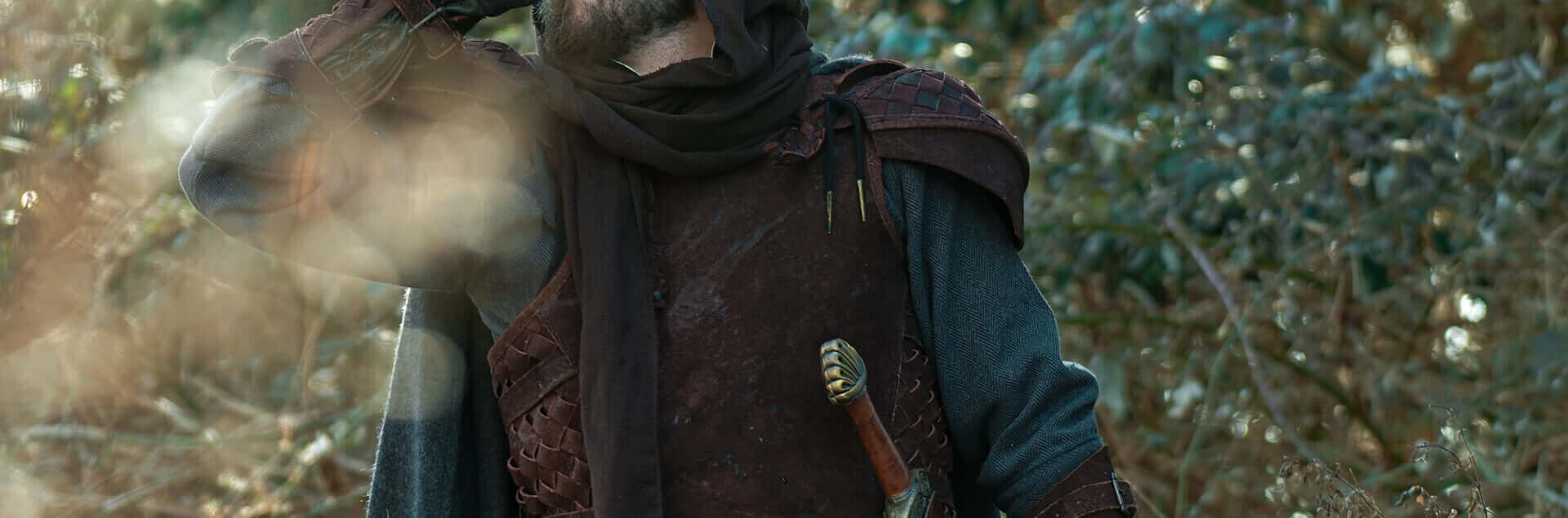 A mysterious figure in medieval attire, gazing into the distance, surrounded by nature.