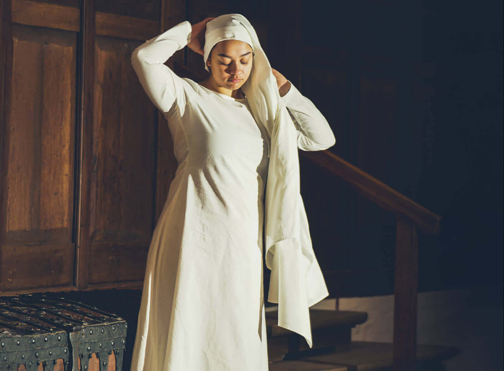 Woman in white medieval dress and head covering, adjusting clothing.