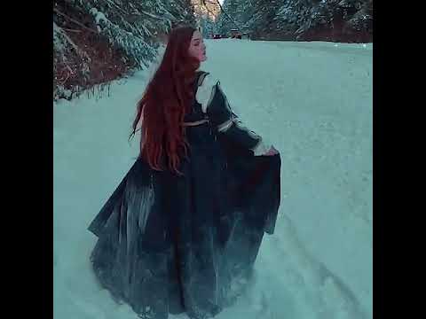 A woman in the snowy forest wearing a flowing Dress Lucrezia, showcasing its elegant design and golden trimmings.