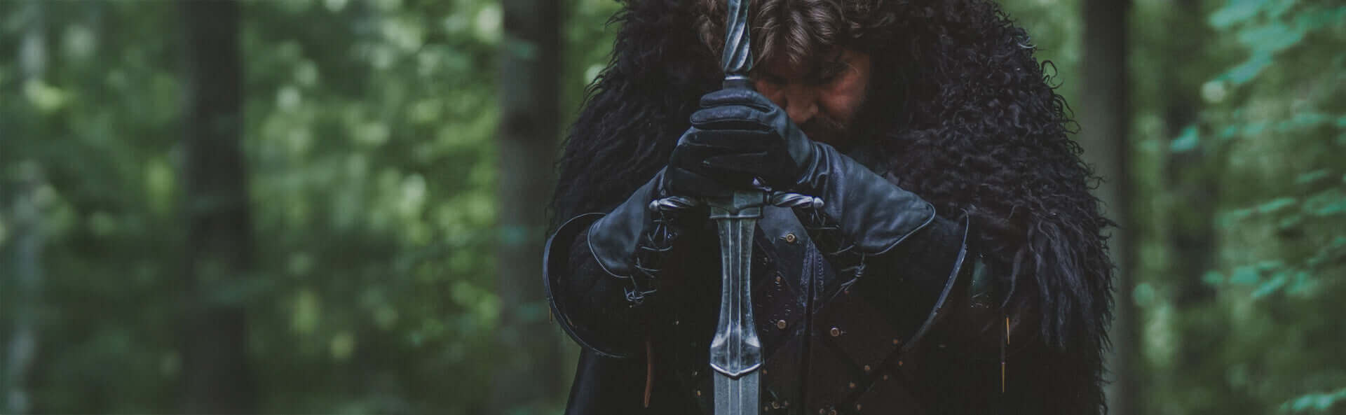Person in dark clothing holding a sword in a forest setting