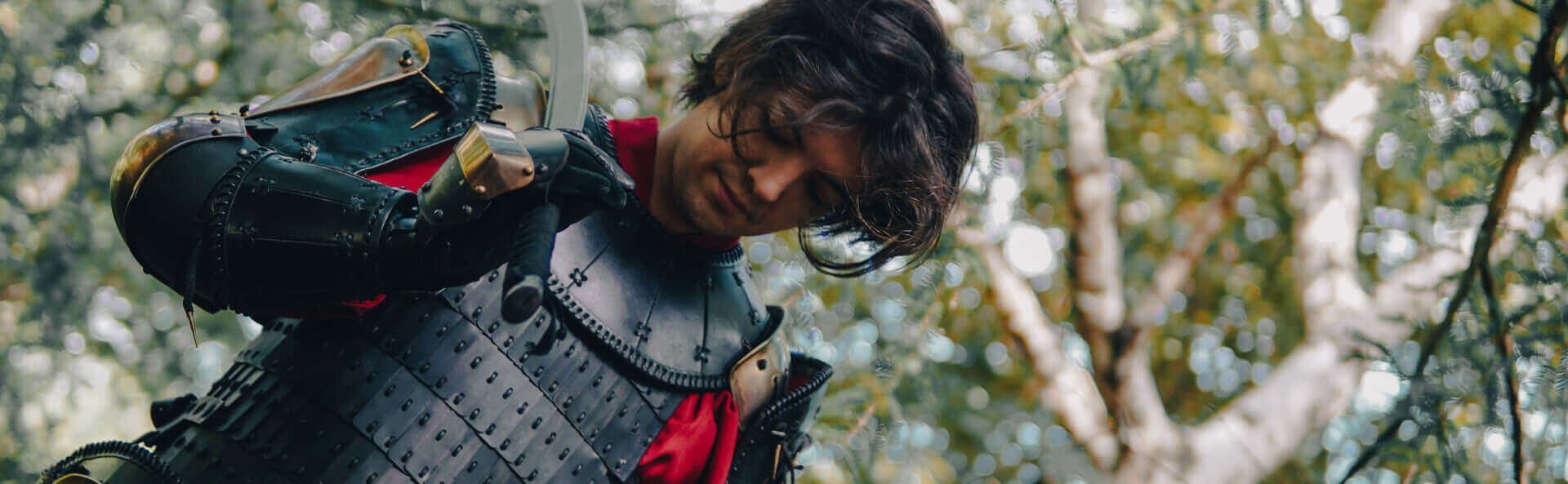 Person in dark armor , holding a sword, in a forest setting.